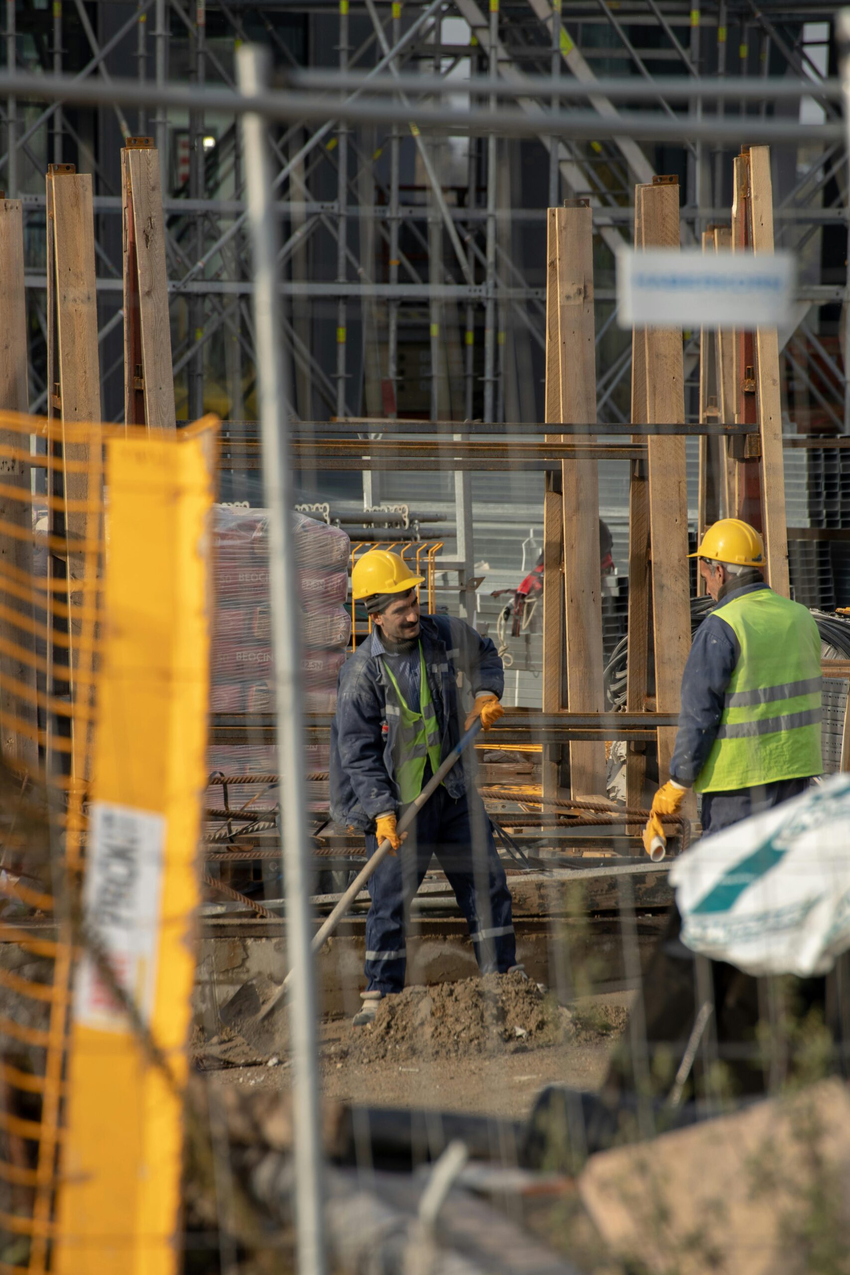 Construction workers in hard hats at an active building site with safety barriers.