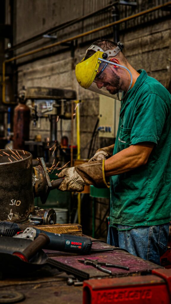 Welder wearing protective gear sparks metal in an industrial setting, showcasing skilled craftsmanship.