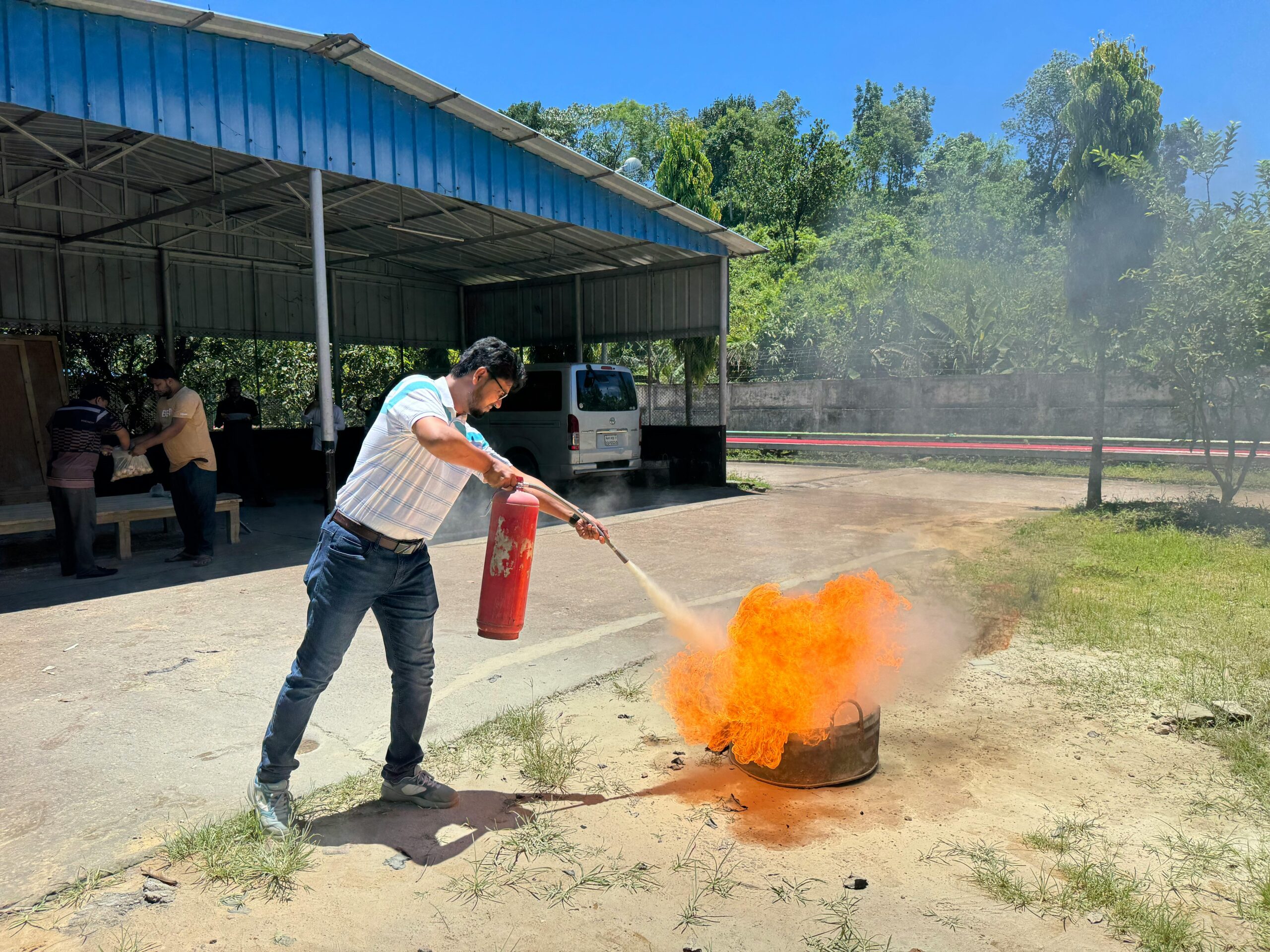 A man uses a fire extinguisher to put out a controlled fire during an outdoor safety training session.