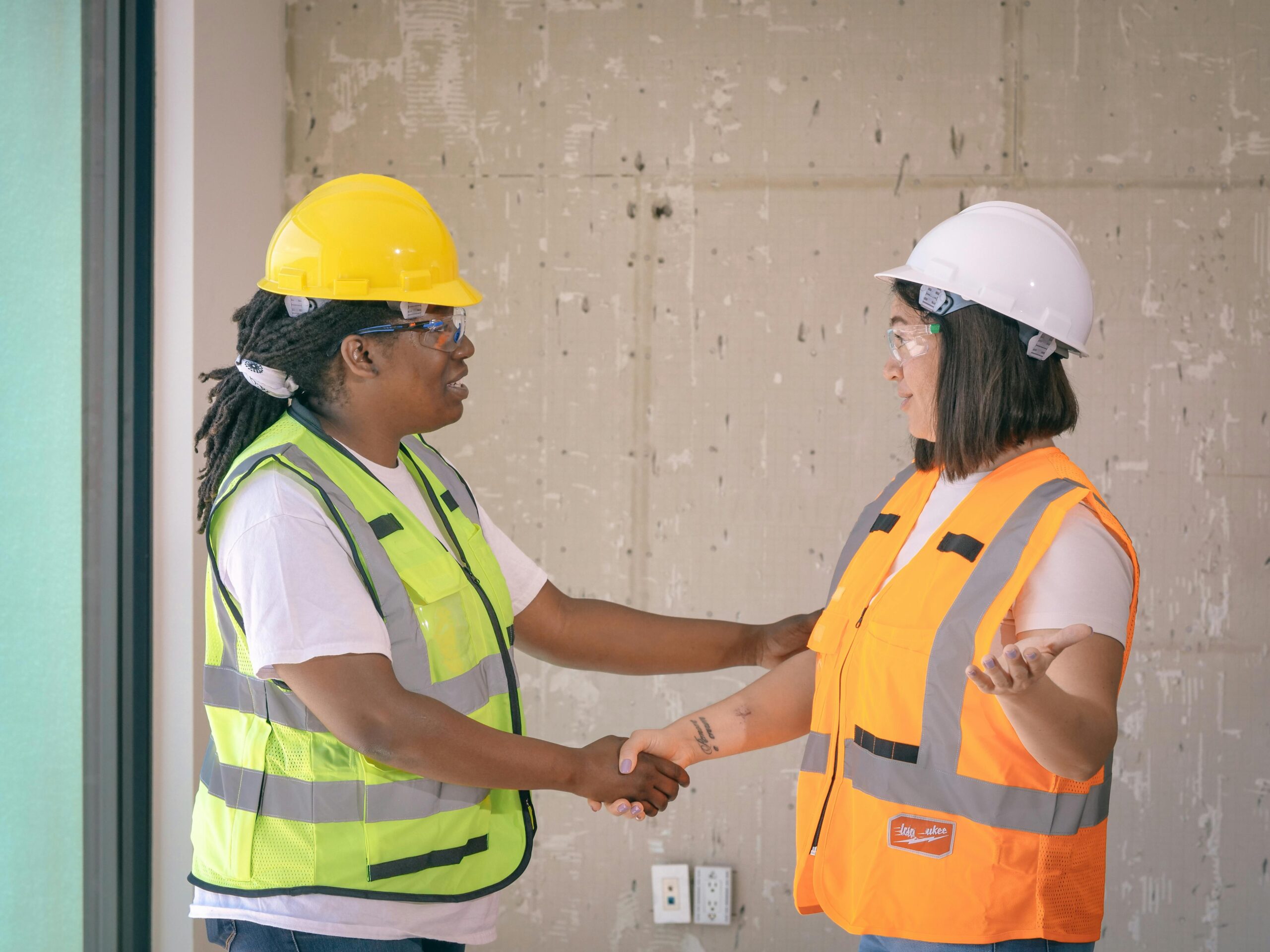 Two construction workers in safety gear shaking hands, symbolizing agreement.