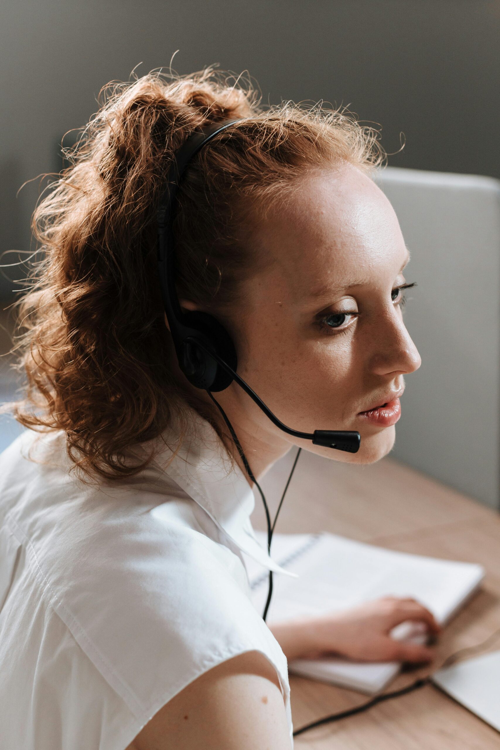 Professional woman at a work desk using a headset, focused on tasks.